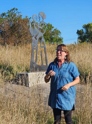 Artist Kacey Koski stands in front of a statue depicting the family members of miners.